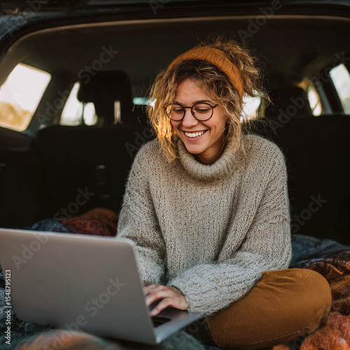 A cheerful woman uses her laptop in her car's trunk.  