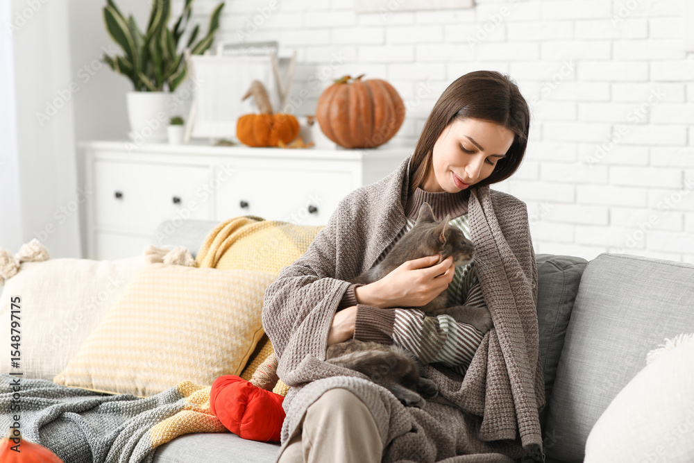 Obraz premium Young woman with warm plaid and grey cat on sofa at home