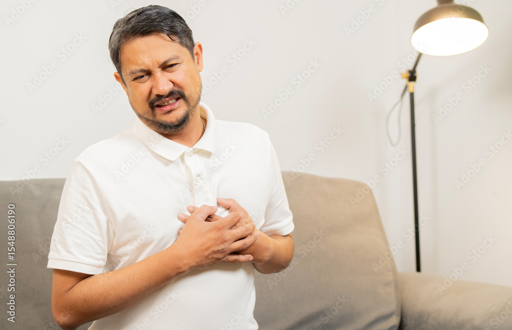 Obraz premium Mature Asian man sitting on sofa clutching and having chest pain cause from heart attack.