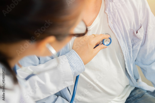 Female middle-aged doctor using stethoscope to examine patient in the hospital.