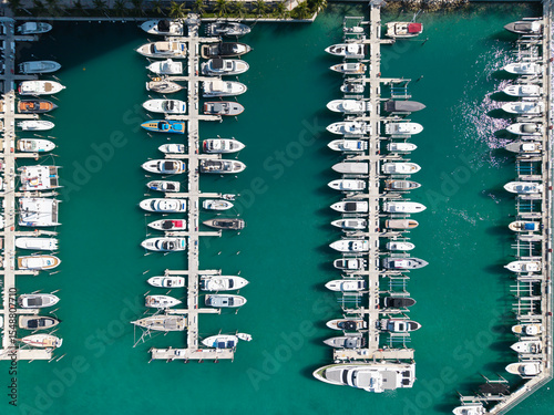 Aerial view of luxury yachts docked at marina. Top-down drone shot of yachts. Boats and sailboats line the scenic seashore. Yacht cruising along the coastline. Harbor filled with vessels at dawn.