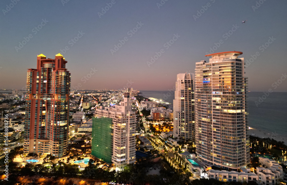 Obraz premium Miami Beach sunset aerial view. Downtown Miami skyline at dusk. South Beach neon lights at night. Tropical Miami waterfront panorama. Ocean Drive Art Deco buildings. Aerial view of Miami coastline.
