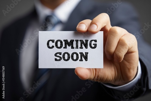Man in a suit holding a card that says COMING SOON