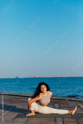 Athletic woman doing gymnastics yoga asana on the beach by the sea