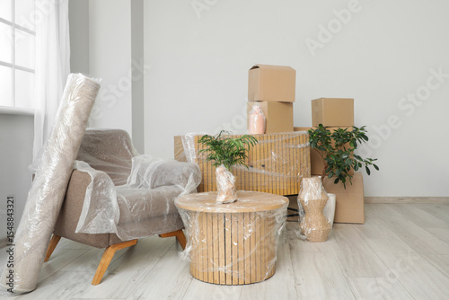 Photos Wrapped furniture with stretch film, plants and boxes in room on moving day
