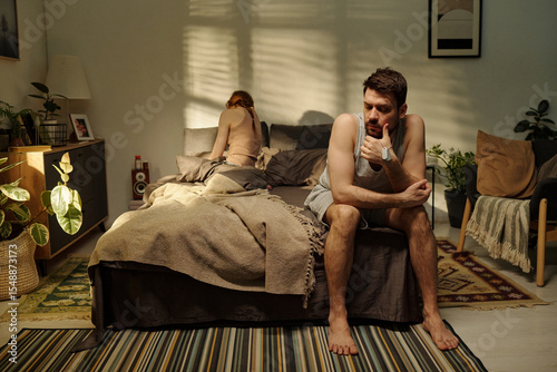 Fotografia Man sitting on bed looking away with thoughtful expression while woman sitting o