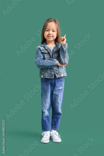 Cute little girl pointing at something on green background