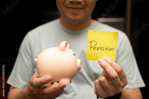 Man Holding Pension Note and Piggy Bank. A smiling man holds a piggy bank and a yellow sticky note with Pension text. saving for retirement and future financial security.