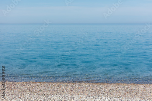 The ocean is calm and clear, with a few rocks on the shore