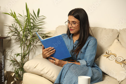Pretty Young woman sitting on cozy couch sofa and relaxing in her living room reading book in Lifestyle Concept
