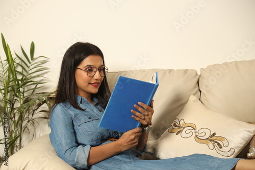 Pretty Young woman sitting on cozy couch sofa and relaxing in her living room reading book in Lifestyle Concept