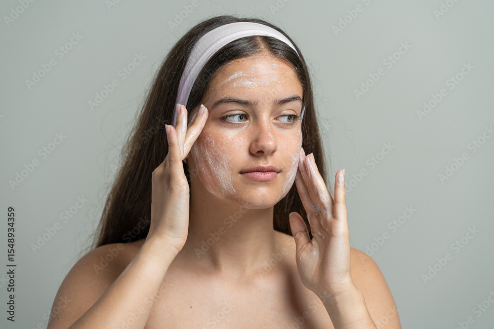 Beautiful woman looking at camera while washing her face with a cleansing scrub or mask Beautiful woman looking at camera while washing her face with a cleansing scrub or mask