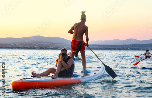 young mens  riding  on sup surfing in the sea at sunset