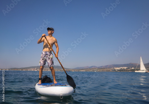 young men  riding  on sup surfing in the sea at sunset