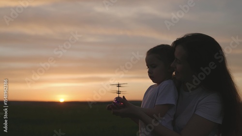 child with mom launch a toy helicopter at sunset into the sky, educational toys for the development of child thinking, happy family concept, motherly care hugging kid, teamwork.