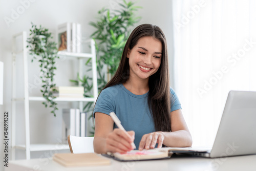 Asian attractive woman taking notes on book while learning from home. 