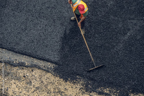 Workers lay a new asphalt coating using hot bitumen. Work of heavy machinery and paver. Top view
