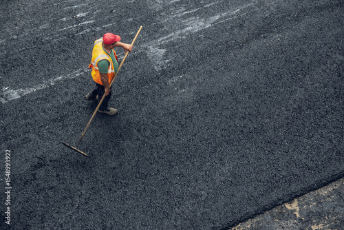 Workers lay a new asphalt coating using hot bitumen. Work of heavy machinery and paver. Top view