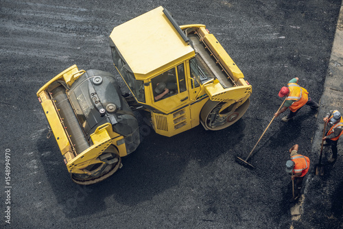 Workers lay a new asphalt coating using hot bitumen. Work of heavy machinery and paver. Top view