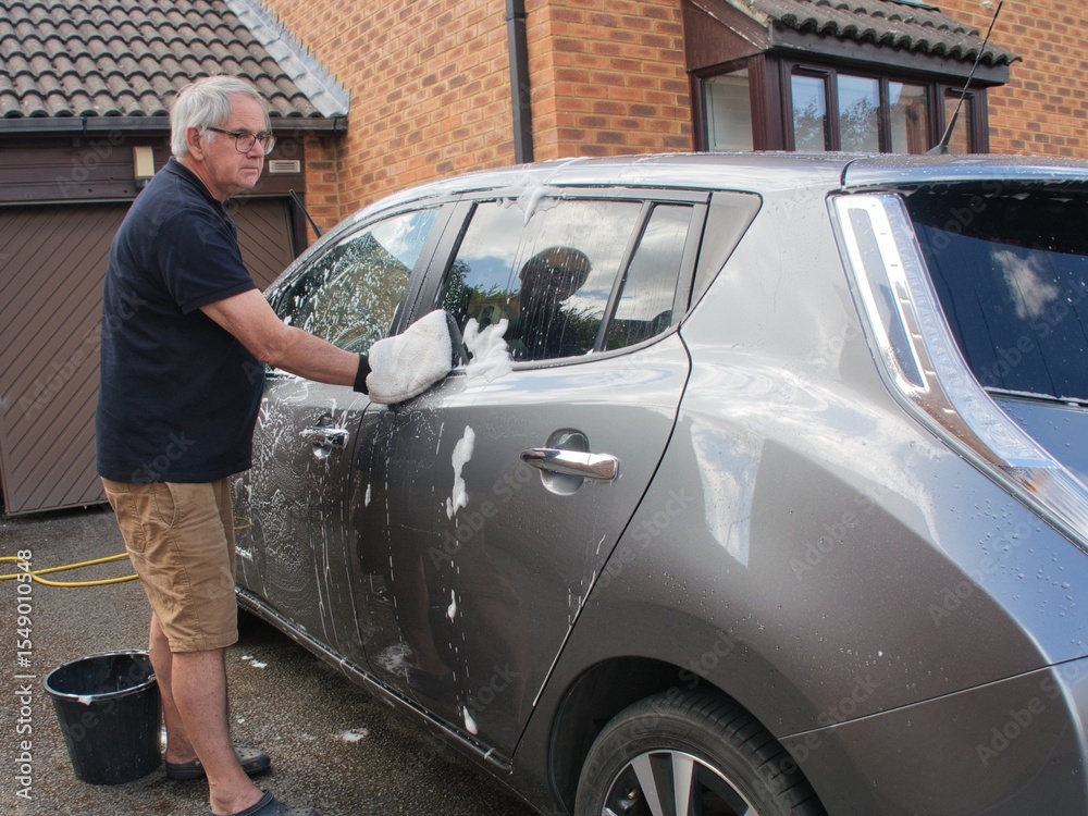 Man washing a silver car with a hand glove in a driveway at home Man washing a silver car with a hand glove in a driveway at home