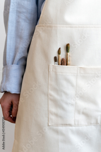 Woman standing with paintbrushes in the pocket of her apron