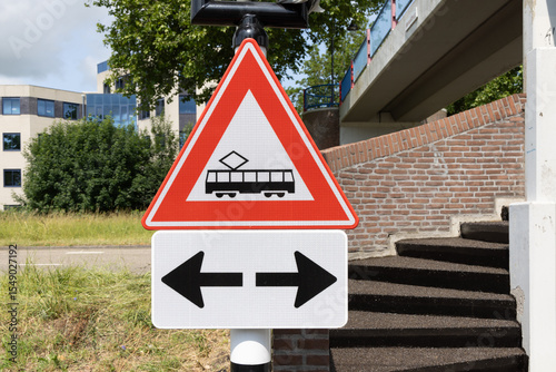 A prominent red and white warning sign for a tram crossing, with arrows indicating directions.