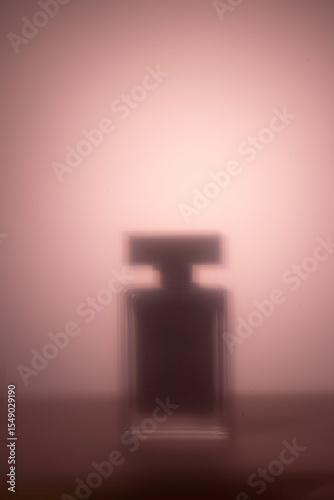 A blurred silhouette of a perfume bottle set against a soft pink gradient background abstract fragrance and beauty concept