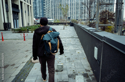 Rear view of a man walking with a backpack along a city path beside modern buildings.