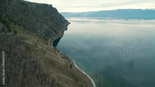 A spring landscape of Lake Baikal with a view of clearwater and a railway with a train at the foot of the hills