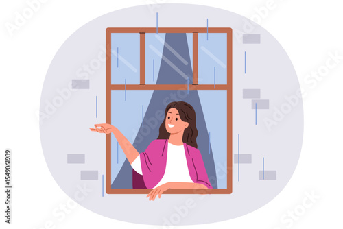 First autumn rain brings joy to woman looking out of apartment window and catching drops with smile. Happy girl enjoying view of street during rain, standing with blanket on shoulders in cozy home