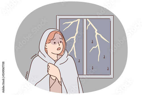 Woman was frightened by lightning and storm outside window wrapped herself in blanket