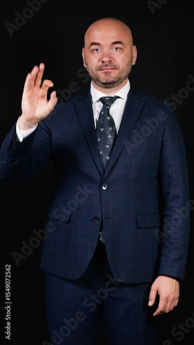 Bald businessman showing ok sign on black background