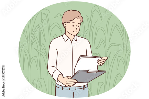 Man farmer inspecting corncobs standing in field with clipboard and working in agribusiness