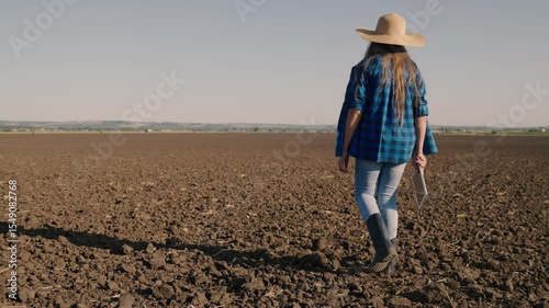 Agriculture, a farmer in rubber boots walks on the plowed land, resting a plot of land after harvesting, an agronomist checks the soil holding a tablet in his hand, agribusiness of fields in the