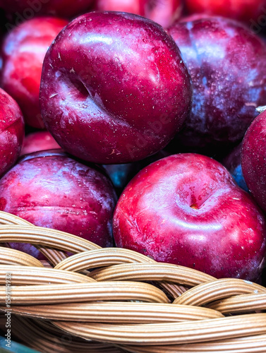 Vertical close-up of large ripe plums in a basket at a farmer's market