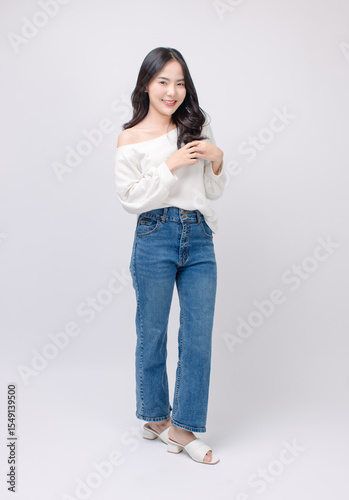 Full body portrait happy smile young asian beautiful woman curly hair wearing long sleeved shirt, blue jeans outfit, casual standing pose on white background joy positivity fashion lifestyle concept.