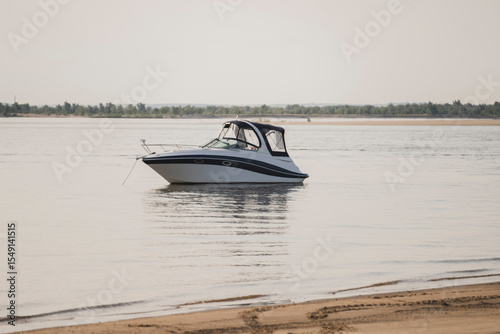 Motor boat anchored near sandy beach at calm waters during late afternoon