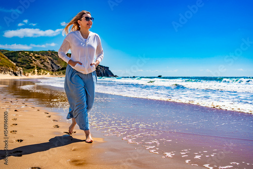 Portrait of beautiful middle aged woman enjoying walk on sandy beach in summertime. Front view. Amado beach on Algarve coast in Portugal	