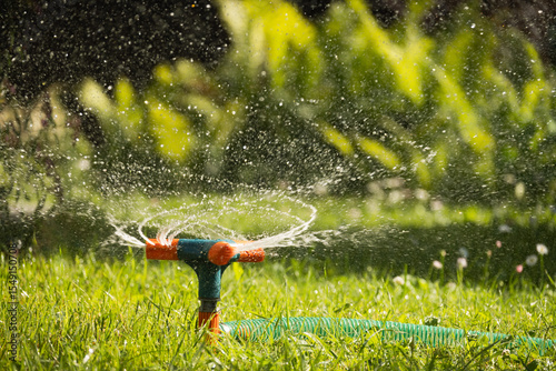 Garden sprinkler watering flowerbed and green lawn with flowers. Watering garden a hose at heat summer. Close up. Automatic smart irrigation system.