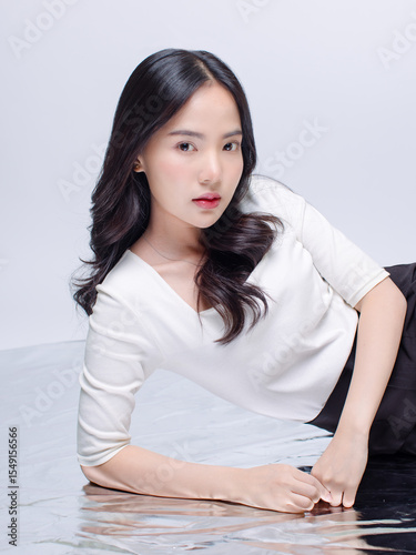 Portrait cheerful young asian beautiful woman curly hair wearing long sleeved shirt, black long pants outfit casual relax on floor in studio laydown on white background joy positivity fashion concept