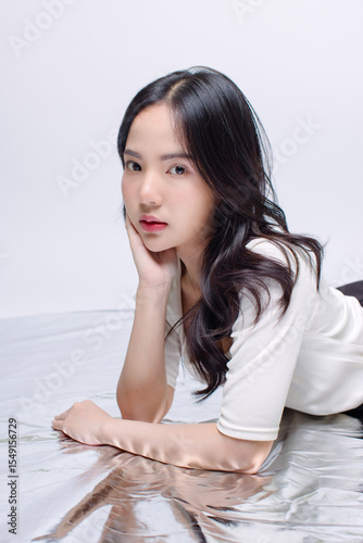 Portrait cheerful young asian beautiful woman curly hair wearing long sleeved shirt, black long pants outfit casual relax on floor in studio laydown on white background joy positivity fashion concept
