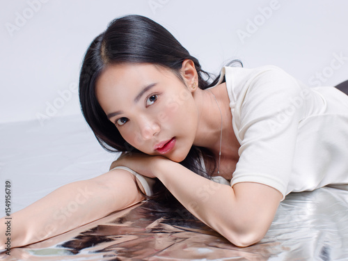 Portrait cheerful young asian beautiful woman curly hair wearing long sleeved shirt, black long pants outfit casual relax on floor in studio laydown on white background joy positivity fashion concept