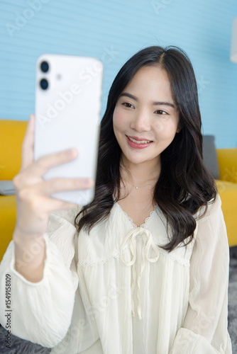 Asian young beautiful happy woman wears casual clothes smile holding using mobile phone, smartphone media, using apps shopping online reading news sitting on floor in light blue living room at home.