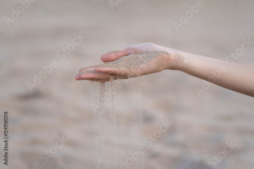Fingers gracefully pouring sand on a beach, capturing fleeting moments of time