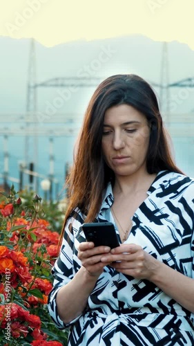 Employee taking notes on work. Girl's hand using smartphone typing a message. Flowers. Electrical substation. Horticultural farm. Agricultural enterprise. Field of roses. Sunset. Specialist.