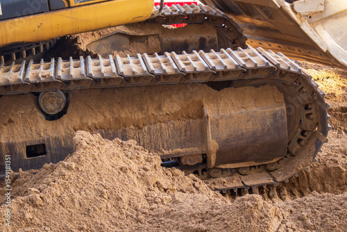 Large piece of machinery with a yellow and black color scheme is sitting in the sand. The machine has a large, muddy tire and tracks