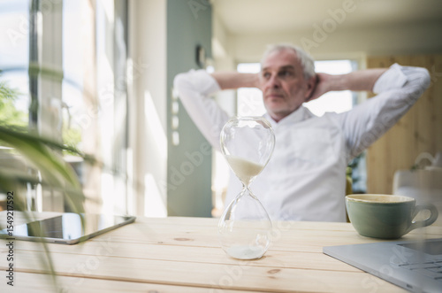 Hourglass on table with senior man sitting in background at home photo