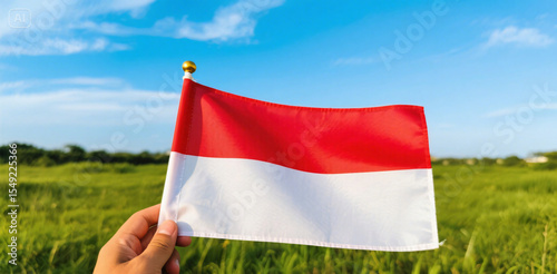 Hand with national patriotism, holding the waving flag of Indonesia country, a symbol of the nation against the sky