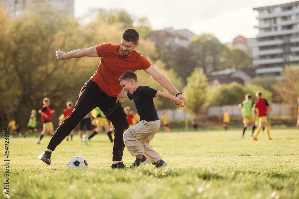 Fototapeta premium Learning how to play soccer. Father and son are having fun outdoors