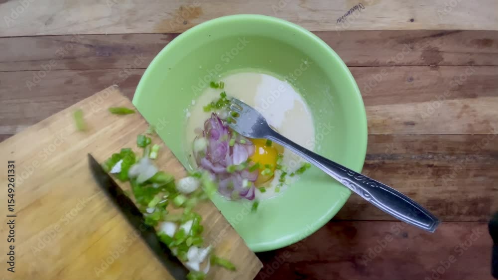 footage of pouring sliced ​​shallots and spring onions into the omelet mixture in green bowl